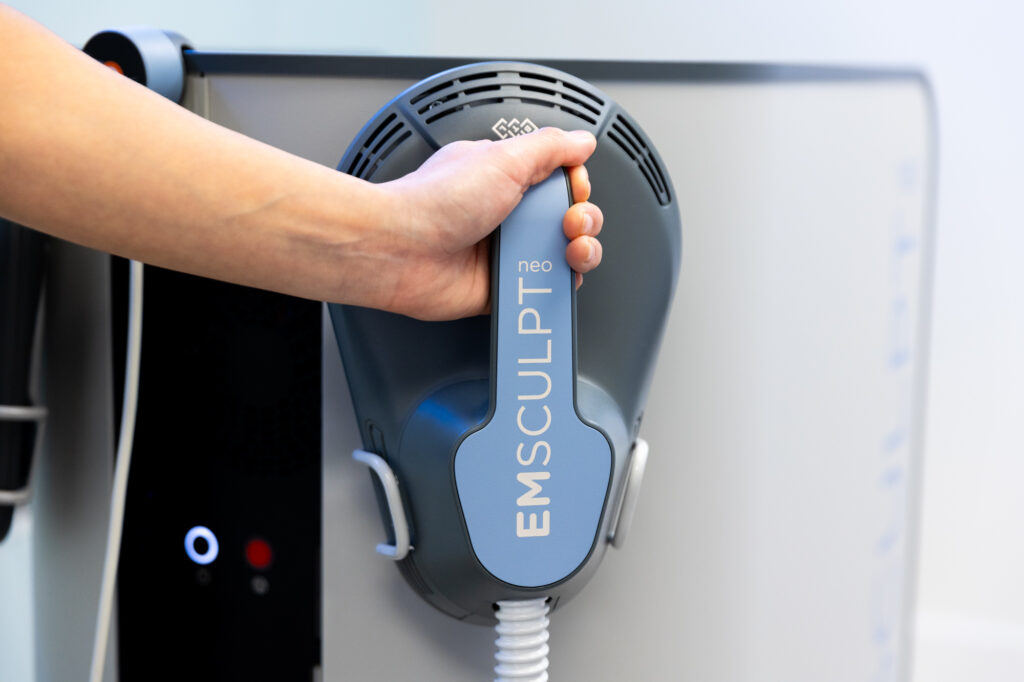 A provider's hand reaches for the Emsculpt device in preparation for treatment with Emsculpt in Miami Beach.